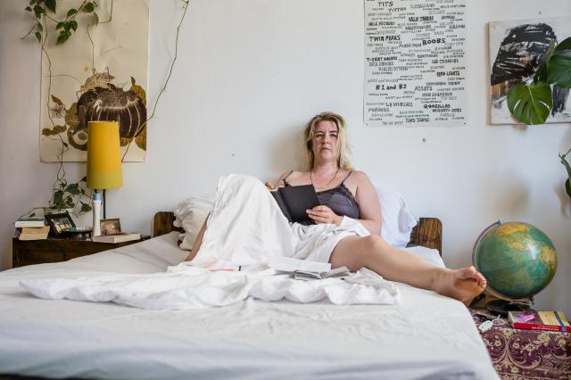 Woman is sitting on a bed with a notebook in her hand. Posters and plants on the background wall