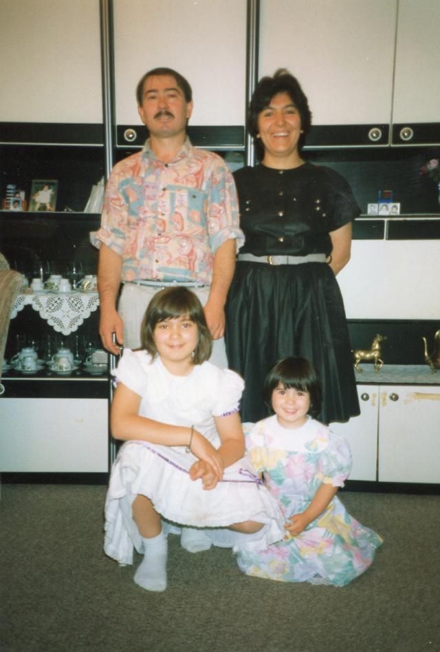 What looks like a family of four (mother, father, two kids) stand smiling looking at the camera, in the background objects in glas furniture.