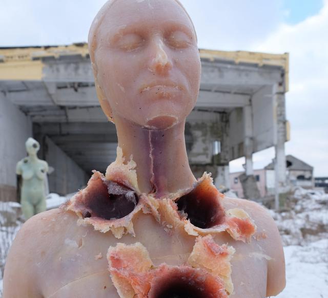 Two sculpture of the female torso with holes as if they were shot, are standing outside in an abandoned place in ruins.