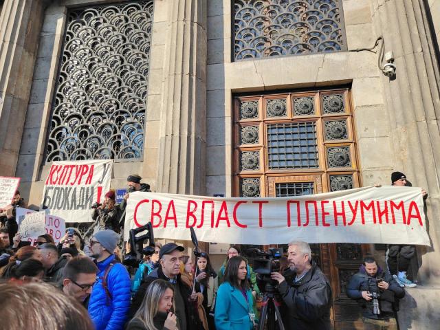 Protesters holding a banner in front of an olde building.