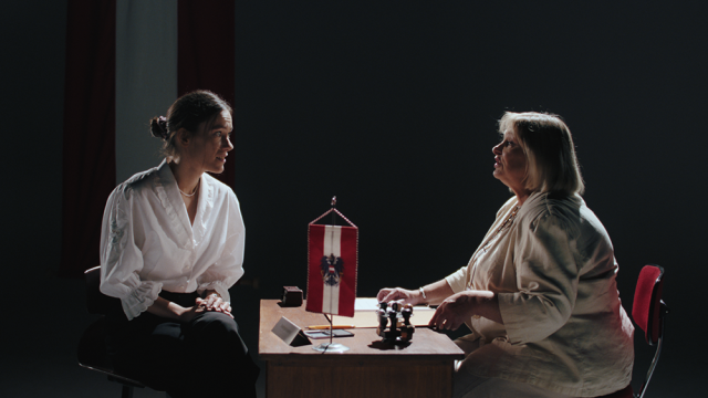 In einem Büro einer Institution sieht man eine ältere Frau auf der einen Seite des Tisches und eine junge Frau auf der anderen Seite. 