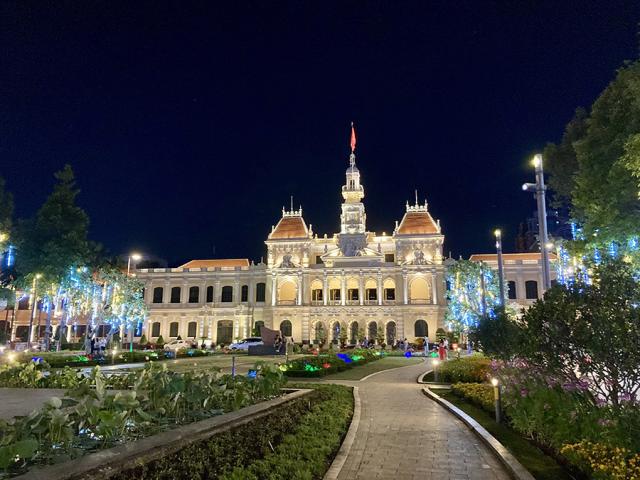 Park mit viel Vegetation und im Hintergrund ein mit bunten Lichtern beleuchtetes Gebäude.