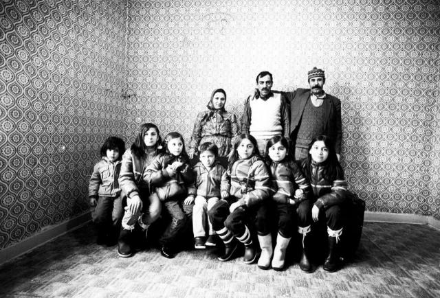 Two men, one woman stand and in front of them 7 kids are sitting.