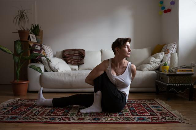 Person is stretching their body while sitting on the floor. There is a couch at the background.