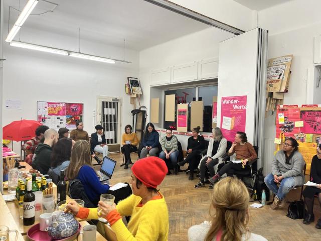 People sitting in circle inside a room. Political banners are displayed on the background.