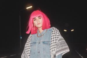 Young girl with pink wig stand on the street at night looking at the camera with strong flash on her body.
